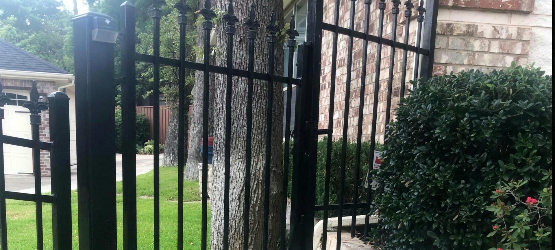 Black ornamental iron fence and walk gate with spear finials beside a stone retaining wall